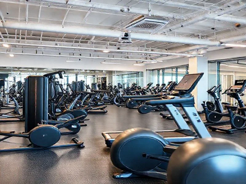A sleek, futuristic cardio machine, possibly a hybrid elliptical/stair climber, rendered in brushed dark metal with sharp, angular lines. It features subtle internal lighting in tactical teal, highlighting specific ergonomic touchpoints and a minimalist holographic display. The machine stands in a sterile, high-tech environment, emphasizing its advanced design and clean aesthetic.